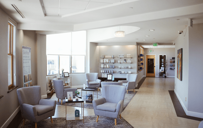 The bright Genesis Colorado Springs clinic lounge with grey seating, product shelves, and large windows.